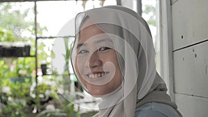 Portrait of beautiful Asian muslim woman smiling at camera, woman stiting relaxing outside her home