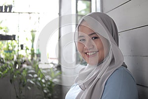 Portrait of beautiful Asian muslim woman smiling at camera, woman stiting relaxing outside her home