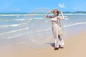 Portrait of beautiful Asian woman with big hat and sunglasses enjoy spending time on tropical sand beach blue sea, happy smiling