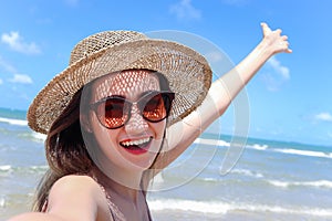 Portrait of beautiful Asian woman with big hat and sunglasses enjoy spending time on tropical sand beach blue sea, happy smiling