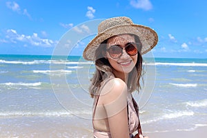 Portrait of beautiful Asian woman with big hat and sunglasses enjoy spending time on tropical sand beach blue sea, happy smiling