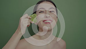 portrait of a beautiful Asian woman doing the procedure with a green gouache quartz stone in the bathroom on a green