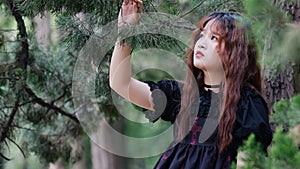 Portrait of beautiful Asian woman posing in summer forest, Chinese girl in vintage black dress looking at trees with blur nature