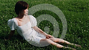 Portrait of beautiful Asian woman sitting on meadows in summer forest, Chinese girl in white dress sleeping with eyes closed