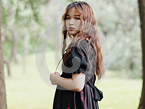 Portrait of beautiful Asian woman standing in summer forest, Chinese girl in vintage black dress looking at camera