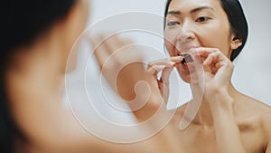 Portrait of Beautiful Asian Woman Uses Dental Floss to Clean Her Natural White Teeth, Smiles in Ba