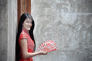 Portrait of a beautiful Asian woman wearing a red cheongsam holding a wooden fan in hand