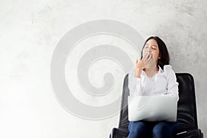 Portrait of beautiful asian young woman yawn at her work place with laptop computer on cement background