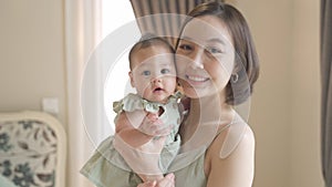 Portrait of beautiful attractive asian woman mother carrying baby infant in bedroom near window at home. short hair mom holding