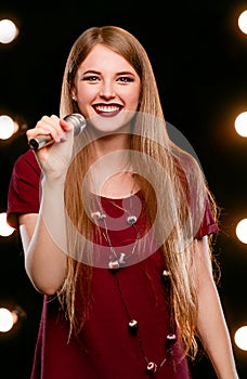 Portrait of beautiful attractive smiling blonde woman singing in microphone in karaoke