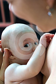 Newborn baby with cute expression is sucking mother`s breast and touching her with soft hand, hungry infant breastfeeding close up