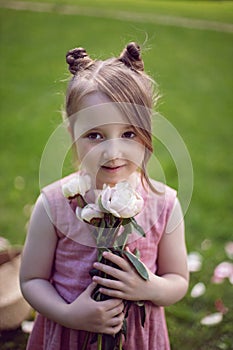 portrait of a beautiful baby girl in a pink dress standing with a bouquet of flowers pions on a green meadow in summer