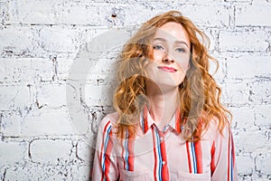 Portrait of a beautiful beautiful young woman student with red curly hair and freckles on her face is leaning against a brick wall
