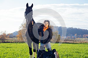 Portrait of beautiful black horse  with his owner and rider  posing in green grass meadow. autumn season