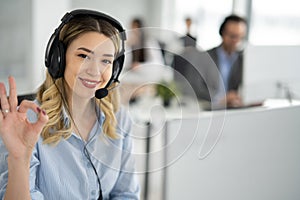 Portrait of beautiful blond haired woman with headset showing OK sing at call centre