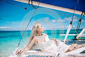 Portrait of the beautiful blond long hair bride in white dress. She lay on the blue sailboat.