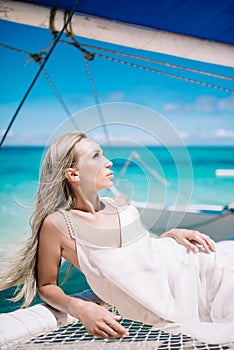 Portrait of the beautiful blond long hair bride in white dress. She lay on the blue sailboat.