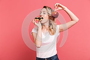 Portrait of beautiful blond woman 20s wearing casual t-shirt holding sweet donut and fresh healthy apple