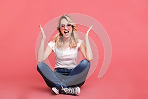 Portrait of beautiful blond woman 20s wearing vintage sunglasses laughing while sitting on floor with legs crossed