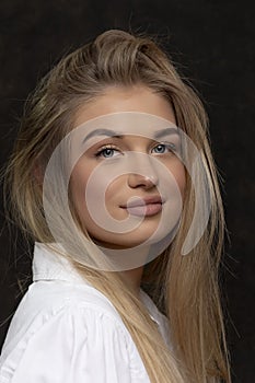 Portrait of a beautiful blonde girl 20-25 years old with long hair on a dark background.