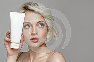 Portrait of a beautiful blonde girl holding a tube of face cream in her hand.