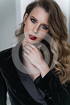 Portrait of a beautiful blonde girl with red lips and evening makeup, wavy hair wearing a black velvet jacket. Healthy, clean skin