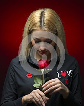 Portrait of a beautiful blonde girl smelling a red rose