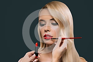 Portrait of beautiful blonde hair girl with visagiste hands applying lipstick with brush,