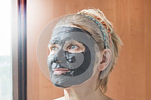Portrait of a beautiful blonde middle-aged woman with a black clay or mud mask on her face, close-up
