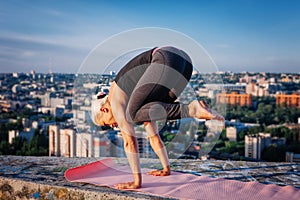 Portrait of beautiful blonde strong woman in sportwear doing workout yoga exercise on the roof of a skyscraper above the big city