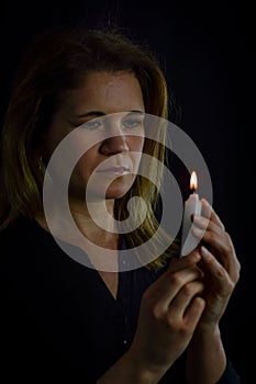 portrait of a beautiful blonde woman with a candle in her hand looking at the flame with hope