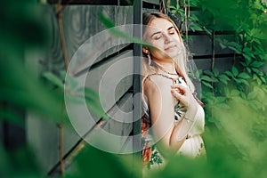 Portrait of a beautiful blonde woman with eyes closed and natural beauty in a green leaves trees on a wooden wall background. Copy