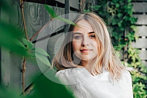 Portrait of a beautiful blonde woman in a green leaves trees on a wooden wall background. Copy, empty space for text