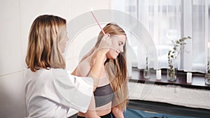 Portrait of beautiful blonde woman receiving ear candle treatment at spa center in slow motion