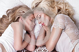 Portrait of the beautiful blonde woman mother and daughter on the beautiful face and amazing eyes lie sleeping on a bed in an eleg