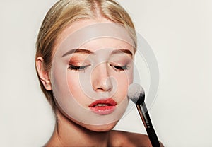 Portrait of beautiful blonde young woman face holding make up brushes. Spa model girl with fresh clean skin  on a white