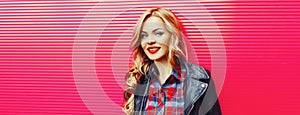 Portrait of beautiful blonde young woman with red lipstick wearing black rock jacket on pink background