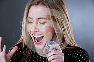 Portrait of a beautiful blonde young woman singing into microphone