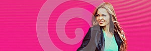 Portrait of beautiful blonde young woman wearing black rock jacket on pink background