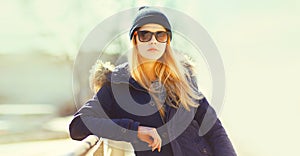 Portrait of beautiful blonde young woman wearing hat, sunglasses and jacket in the city