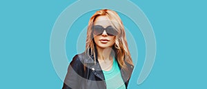 Portrait of beautiful blonde young woman wearing sunglasses, black rock jacket on blue background