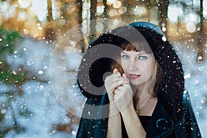 Portrait of beautiful blue-eyed girl in winter forest during snowfall