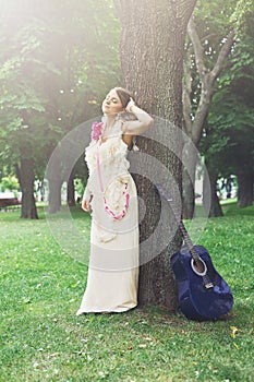 Portrait of beautiful boho girl near tree with blue guitar