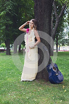 Portrait of beautiful boho girl near tree with blue guitar