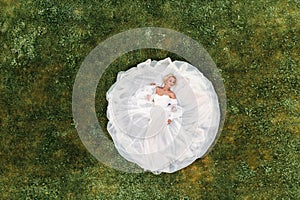 Portrait of a beautiful bride lying on the ground in a white wedding dress.photo of an elegant bride on the green grass.Top photo