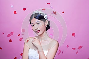 Portrait of beautiful bride with rose petals in mid-air against pink background