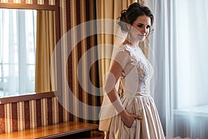 Portrait of a beautiful bride in a wedding dress standing in a room near window