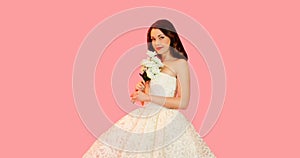 Portrait of beautiful bride woman with bouquet of flowers wearing white wedding dress on pink background