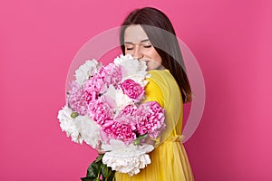 Portrait of beautiful brunette girl standing with closed eyes, looking gentle, brunette woman wearing yellow dress, model