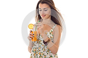 Portrait of beautiful brunette girl in summer sarafan with floral pattern drinks orange cocktail isolated on white